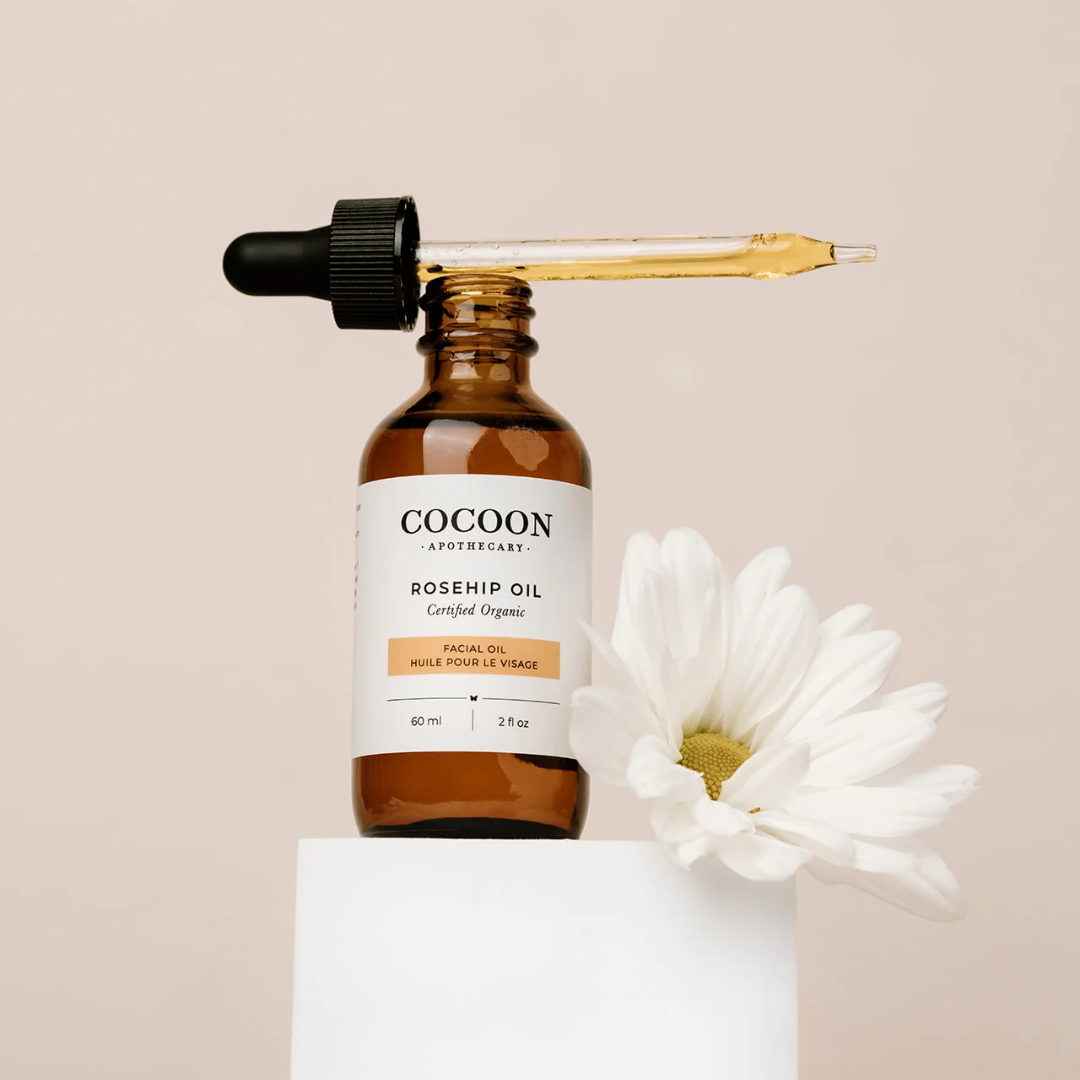 A serum bottle opened with the dropper exposed, next to a white flower.