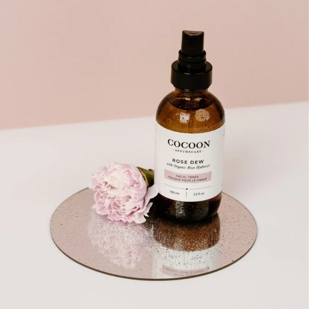 A skin care bottle next to a pink rose